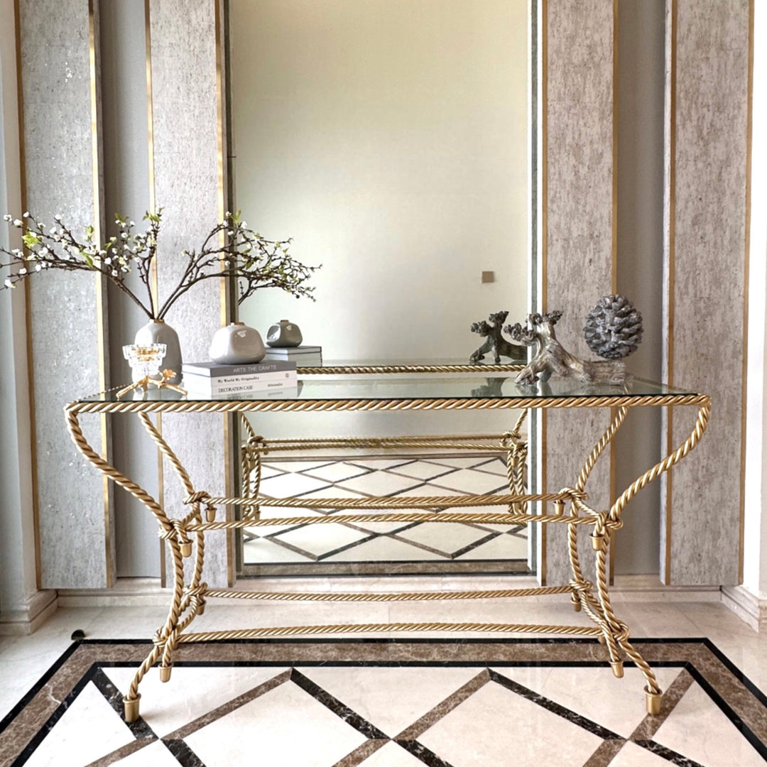 Noura console table with gold rope-inspired metal base and glass top, rich in sculptural detail.