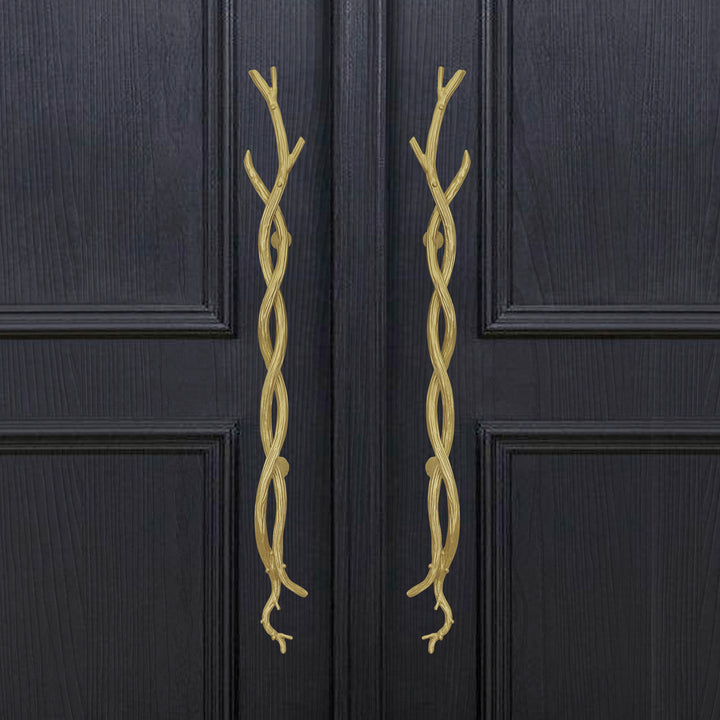 A pair of decorative golden pull handles inspired by twisted branches mounted on a closed wooden door