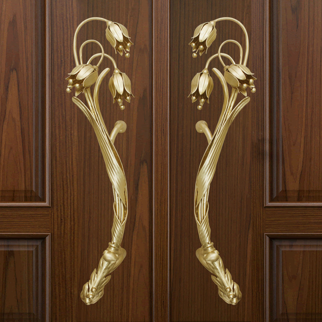 A pair of golden decorative pull handles inspired by the snowdrop flower mounted on a closed wooden door