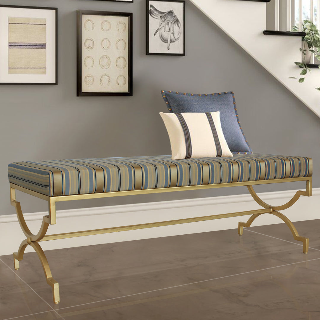 A contemporary metal golden bench topped with stripy blue silk upholstery in a living space