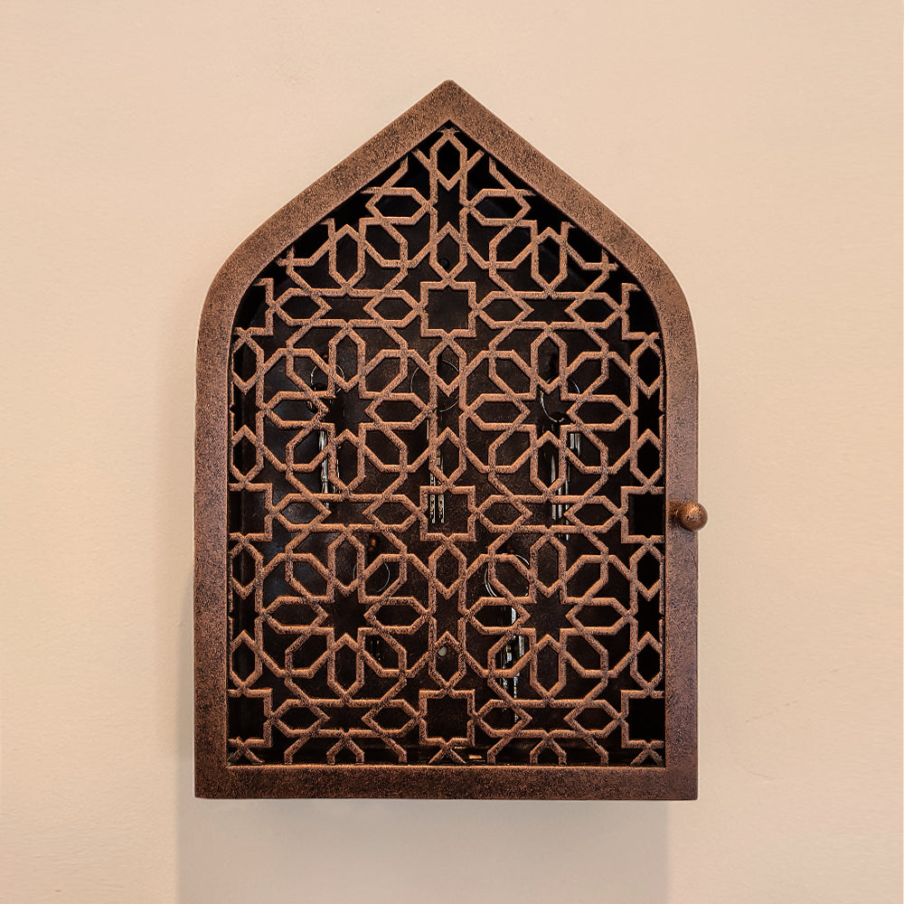 A wall mounted closed key cabinet with a geometric pattern and Islamic arched top painted in an antique bronze finish