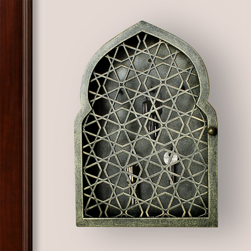 Key cabinet with a geometric pattern and Islamic arched top painted in an antique green-gold finish mounted on a wall beside a wooden door