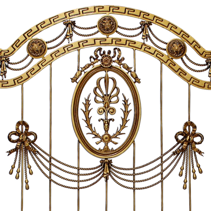Close up of a wrought iron headboard made up of classical elements and a versace pattern, painted in an antique gold color