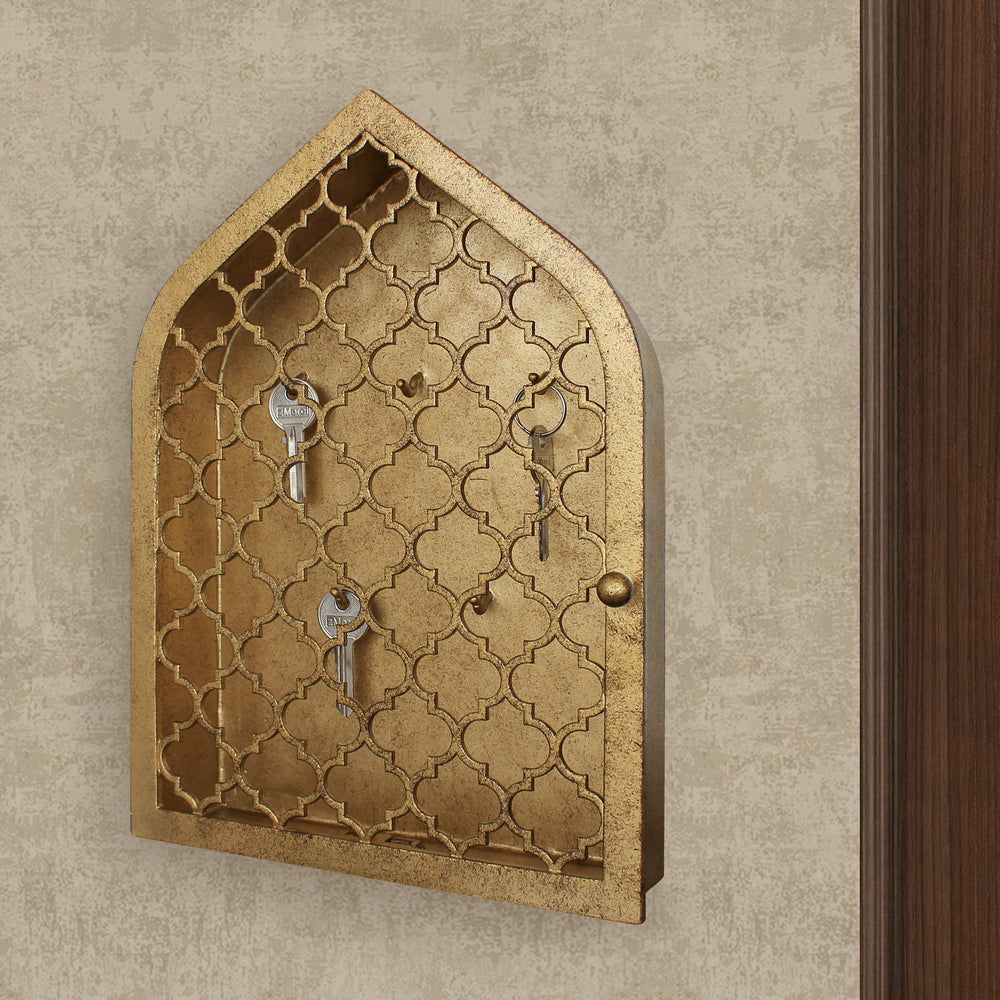 Key cabinet with a quatrefoil pattern and a pointed arched top painted in an antique gold finish wall mounted beside a wooden door