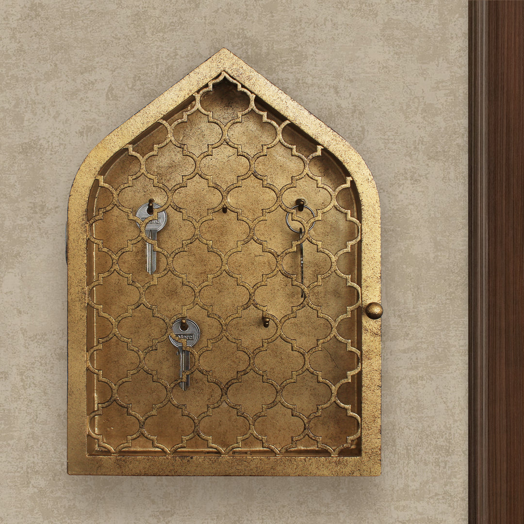 Key cabinet with a quatrefoil pattern and a pointed arched top painted in an antique gold finish wall mounted beside a wooden door