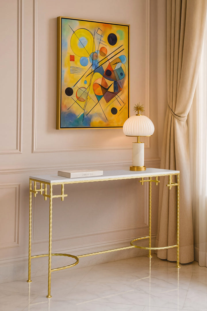Console table with gold frame and marble top in a room with abstract art and lamp.