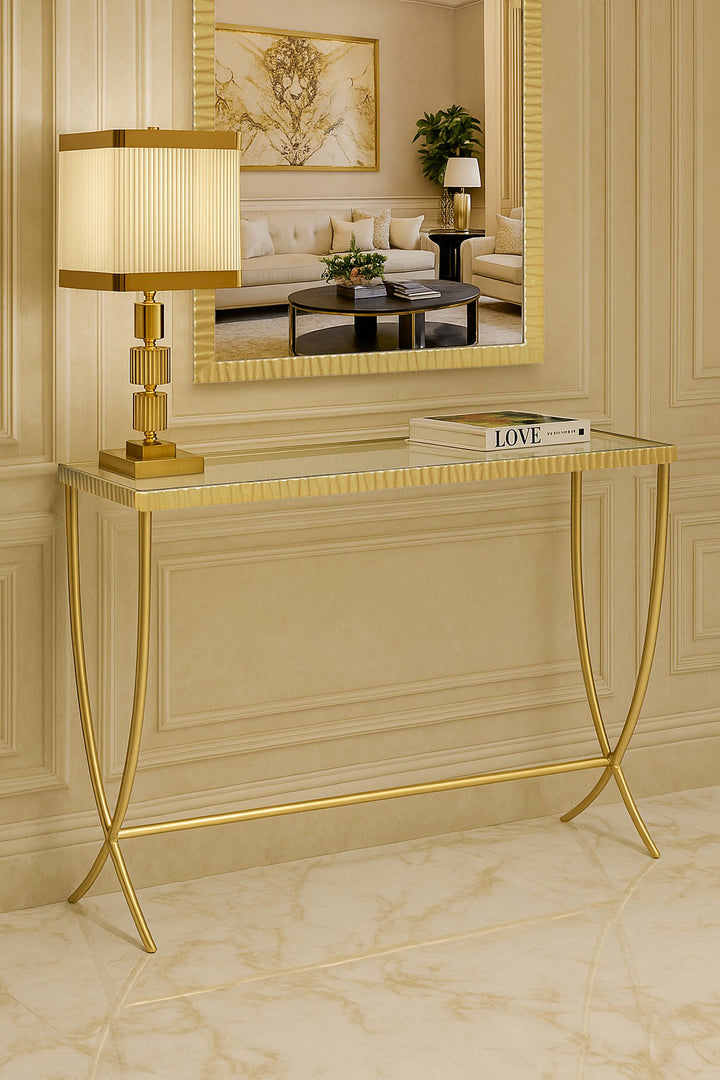 Elegant gold console table with fluted edges and curved legs, styled in a refined beige marble interior with a decorative mirror and lamp.
