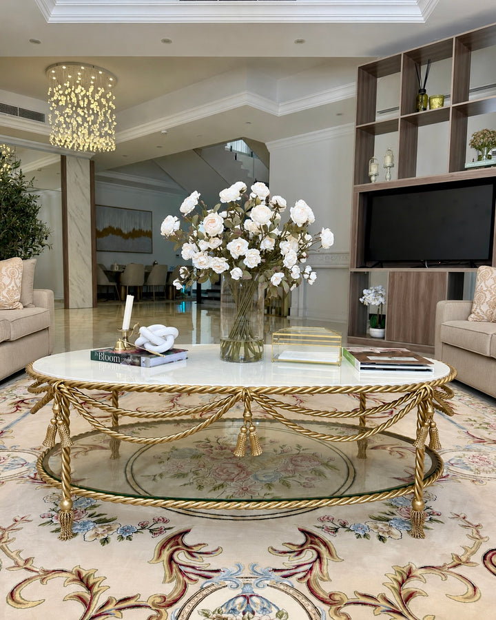 Allegra Oval Center Table featuring a handcrafted antique gold wrought iron frame with twisted rope detailing, white marble top, and tempered glass lower shelf in a luxury living room.