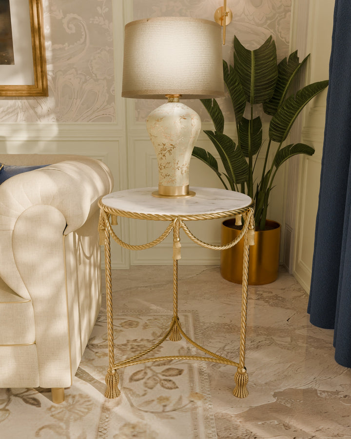 Allegra round side table in gold with marble top, featuring rope-inspired metalwork, styled beside a sofa in an elegant living space.