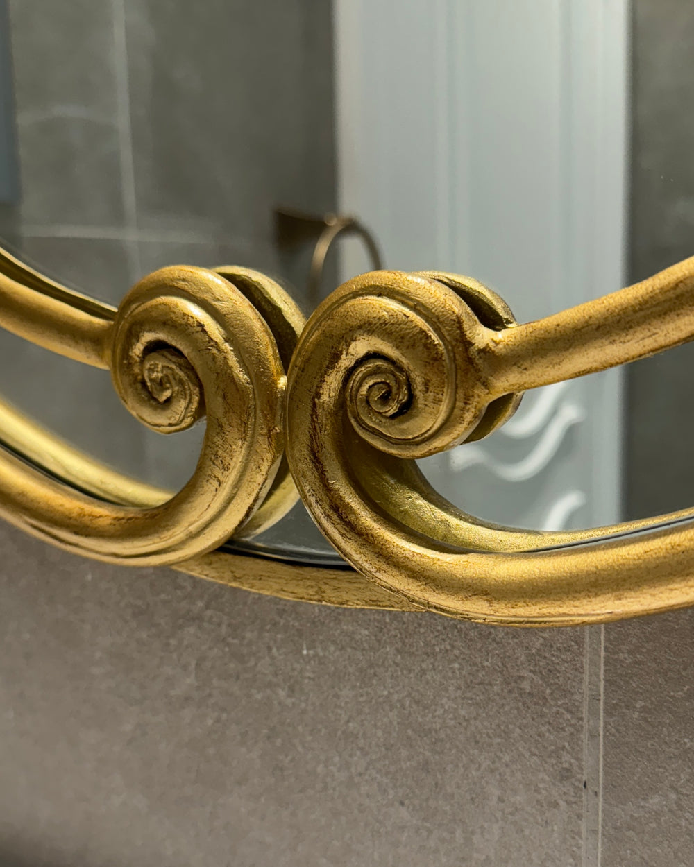 Elegant twin scrolls at the base of the Audrey Mirror with an antique gold patina