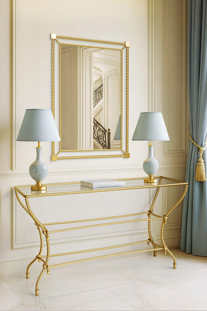 Noura console table in antique gold with rope-inspired metalwork, styled beneath matching mirror in an elegant classical interior.
