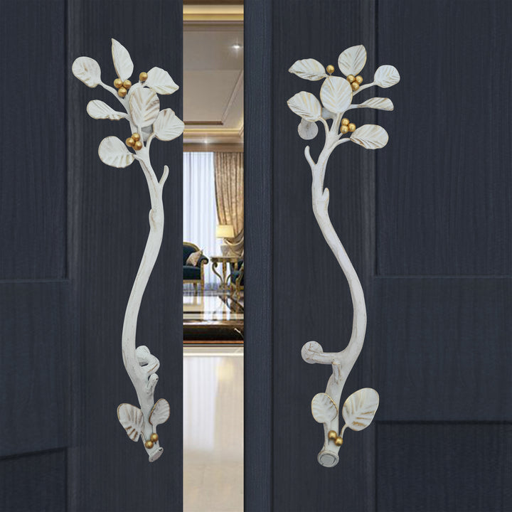 A pair of white and gold decorative pull handles inspired by nature's leaves mounted on an open wooden blue door