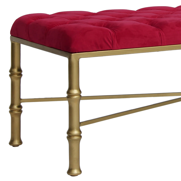 Close up of a unique metal bench with bamboo styled legs, topped with a red velvet tufted cushion