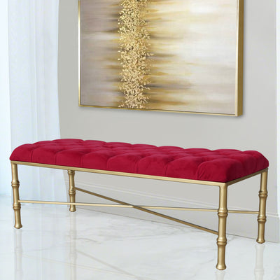 A contemporary metal golden bench topped with red velvet tufted upholstery in a luxurious living space