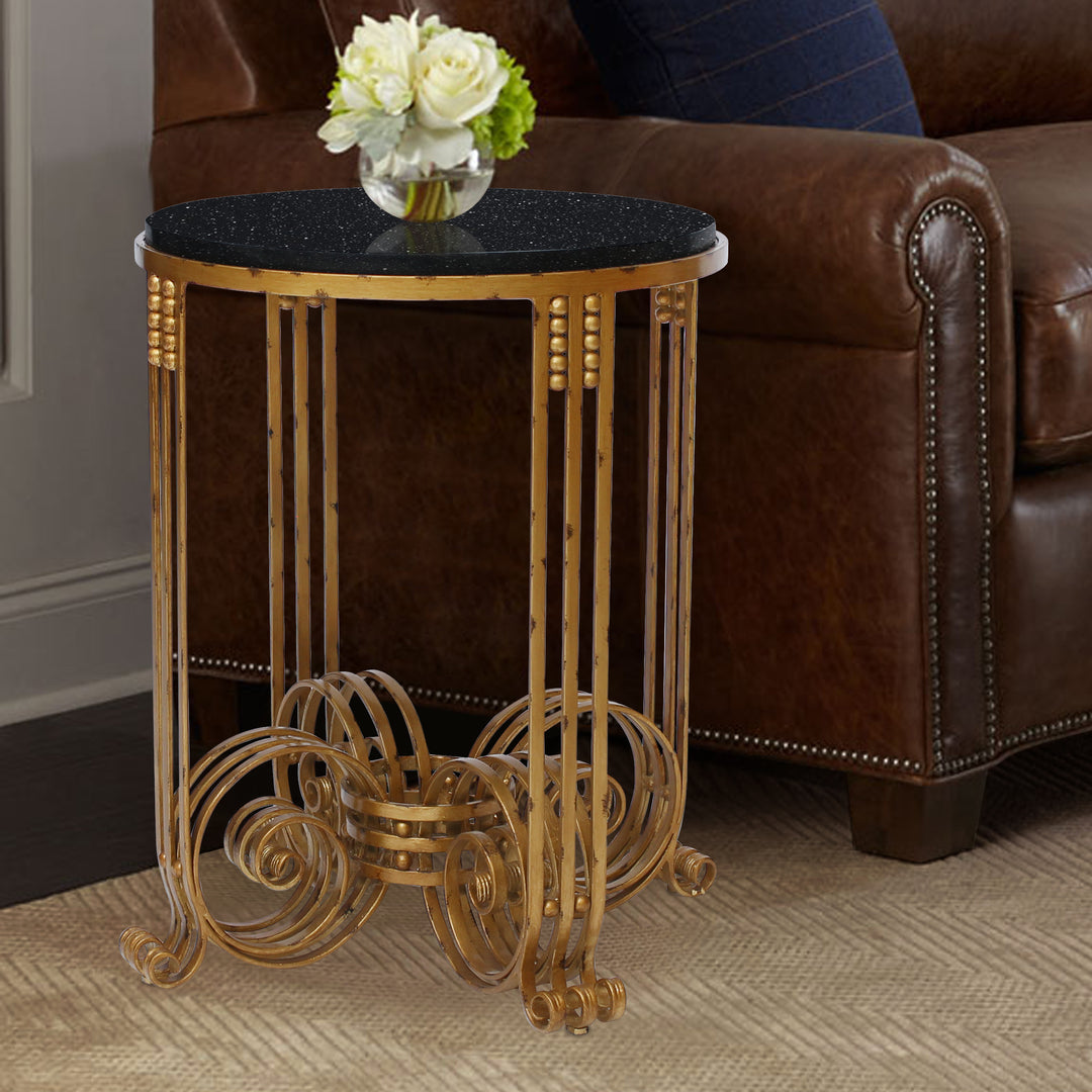 An Art Deco styled end table made of wrought iron and topped with a round black granite stands by a leather couch