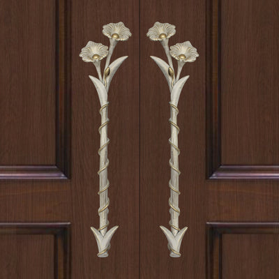 A pair of antique white decorative accent pull handles inspired by flowers mounted on a closed wooden door