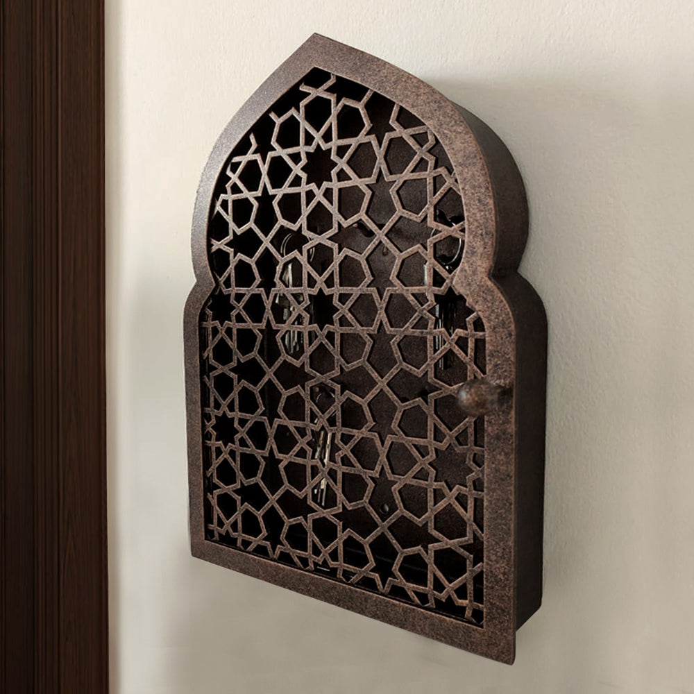 A bronze decorative key cabinet with an Islamic design pattern mounted on a wall beside a wooden door 