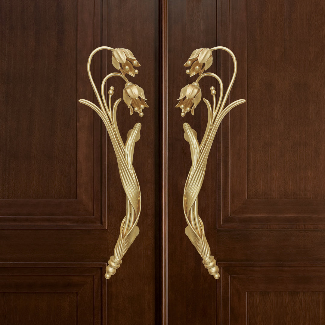 A pair of golden decorative pull handles inspired by the snowdrop flower mounted on a closed wooden door