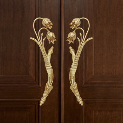 A pair of golden decorative pull handles inspired by the snowdrop flower mounted on a closed wooden door