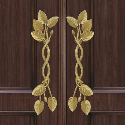 A pair of golden decorative pull handles inspired by branches, leaves and buds mounted on a closed wooden door