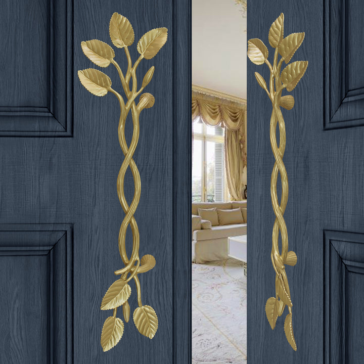 A pair of golden large decorative pull handles inspired by branches, leaves and buds mounted on an opened wooden door