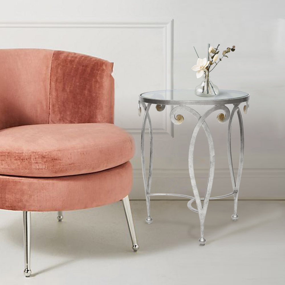An exquisite silver end table made up of metal scrolls stands beside a pink arm chair