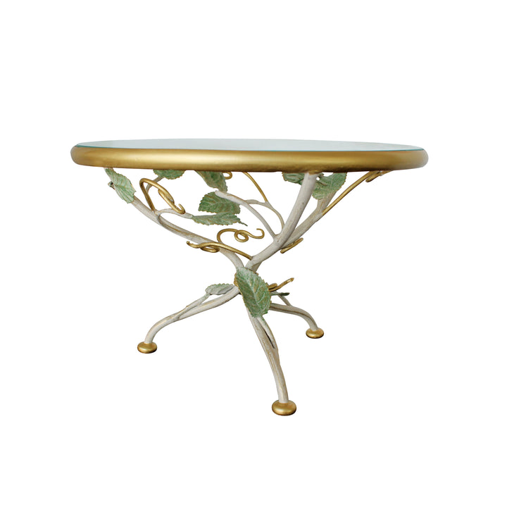 A decorative cake stand with a base adorned with leaves and branches inspired from nature topped with a round clear glass