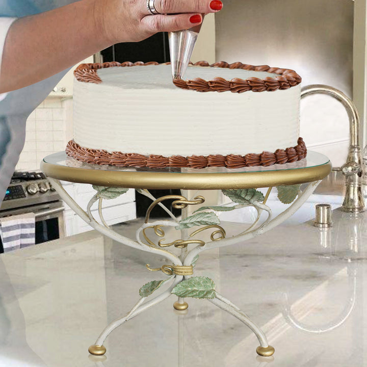 A lady decorates a cake sitting on an decorative stand over a kitchen counter