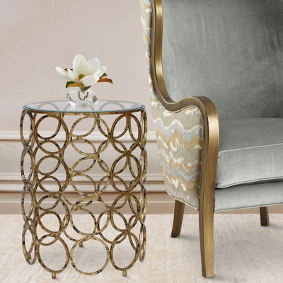 A unique accent table made of a collection of antique golden rings sits beside a classical blue arm chair