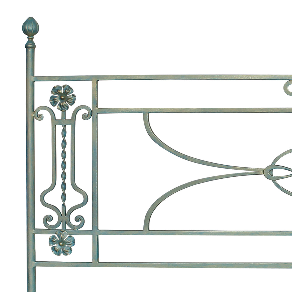 Close up of a simple classical metal headboard with scrolls and flowers painted in a pastel blue color