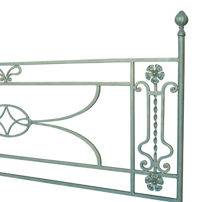 Close up of a simple classical wrought iron headboard with scrolls and flowers painted in a pastel blue color