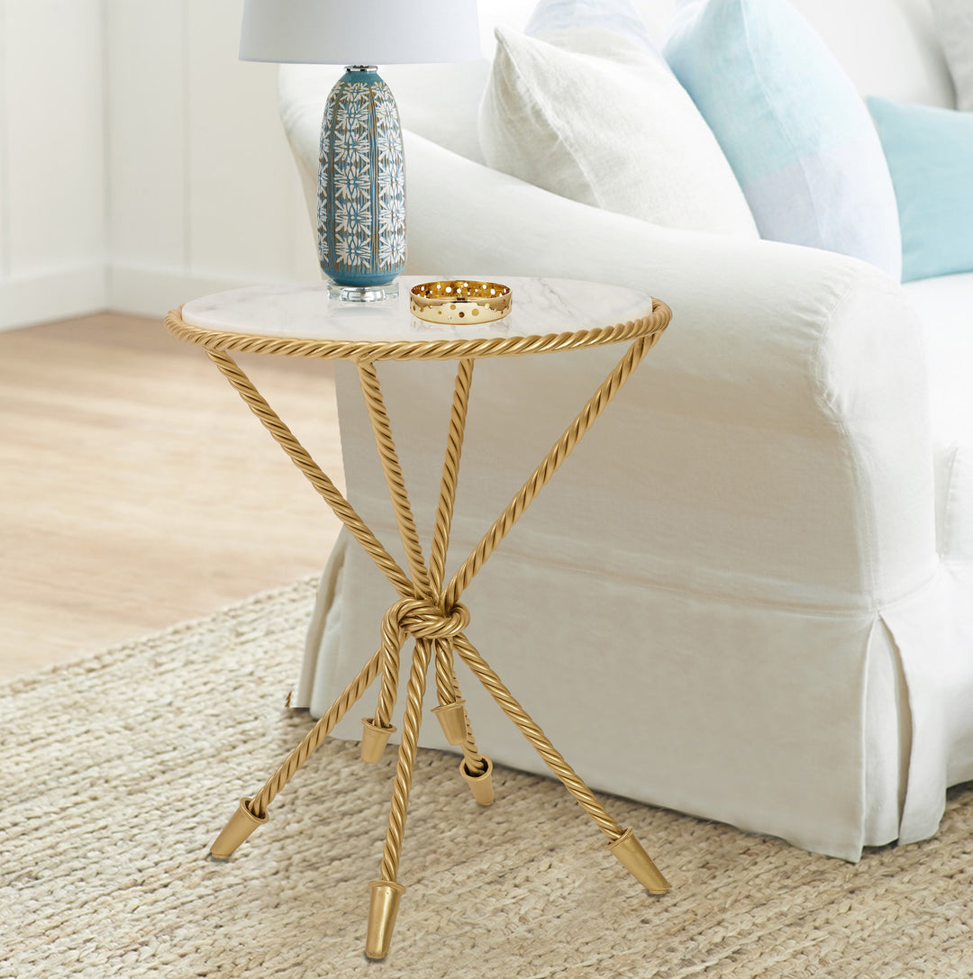 A golden round rope-themed side table with a white marble top stands beside a white sofa