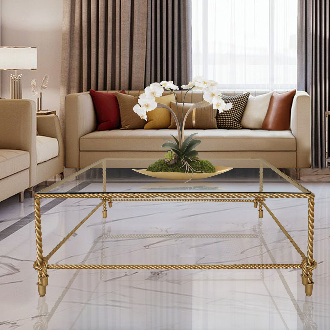 Square coffee table between sofas in a comfortable family room. Golden colored with glass top.