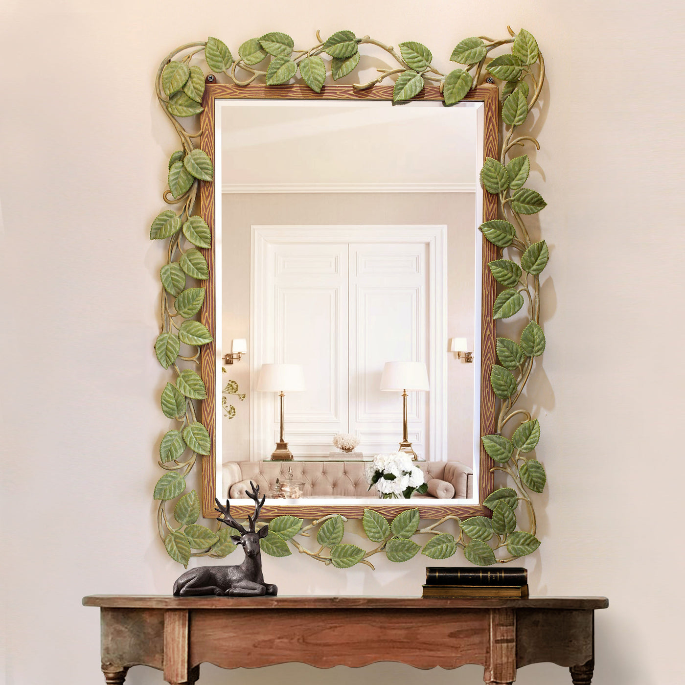 A unique metal rectangular mirror with leaves along its border painted in natural colors; hangs above a console table