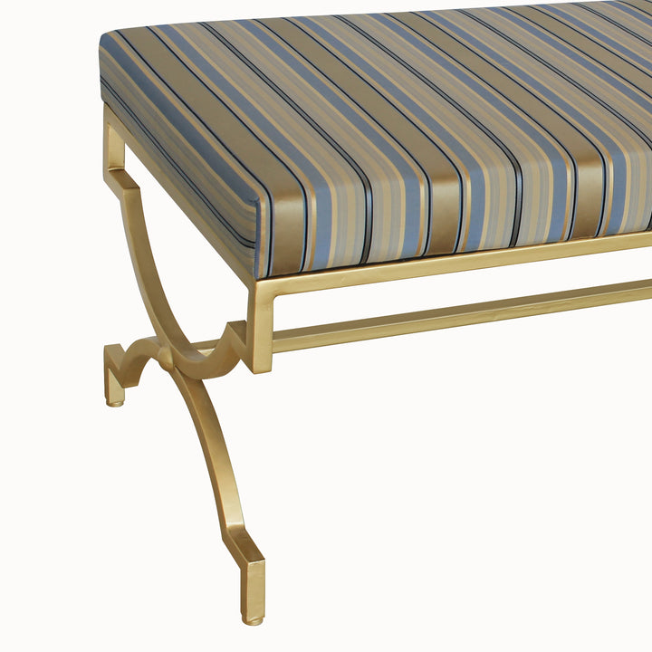 Close up of a modern bench with a geometric metal gold base topped with a stripy silk upholstered cushion