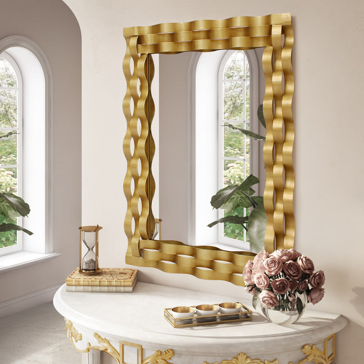 A rectangular golden mirror with wavy strips made of metal wrapped along its border, hangs on a wall above a console table