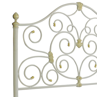Close up of a wrought iron headboard for a single bed with scrolls and classical motifs, painted in white and gold