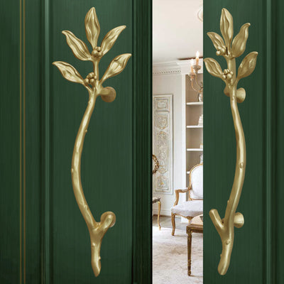 A pair of wrought iron door handles with decorative leaves installed on a half opened door