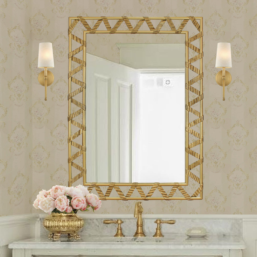 A rectangular golden mirror with a ribbon-like metal strip that forms a zigzag pattern along its perimeter; hangs above a wash basin
