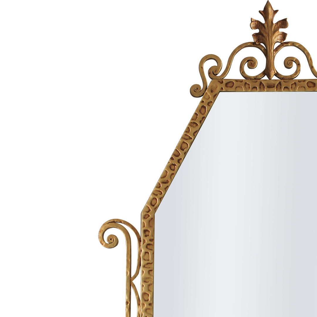 A close up of a classical hand forged mirror with textured scrolls painted in an antique golden finish