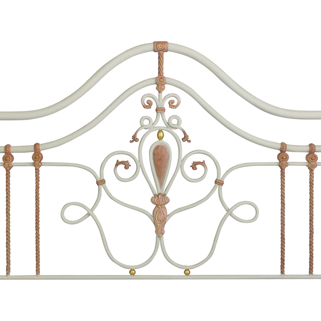 Close up of a wrought iron headboard for a girls single bed with scrolls, leaves and motifs painted in white, pink and hints of gold