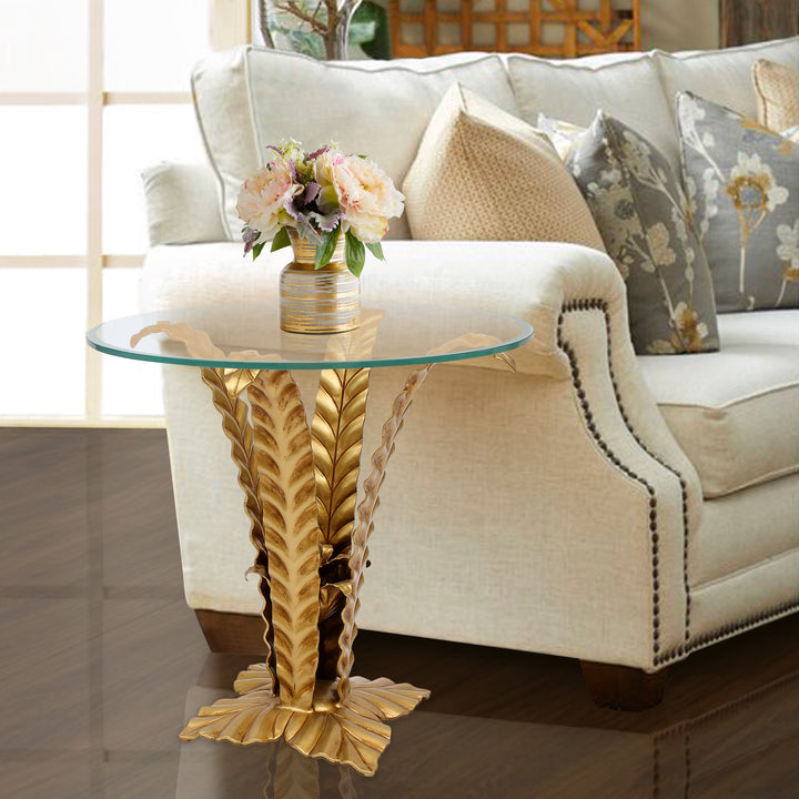 An eclectic side table with golden leaves that branch out to hold a piece of clear glass by a sofa