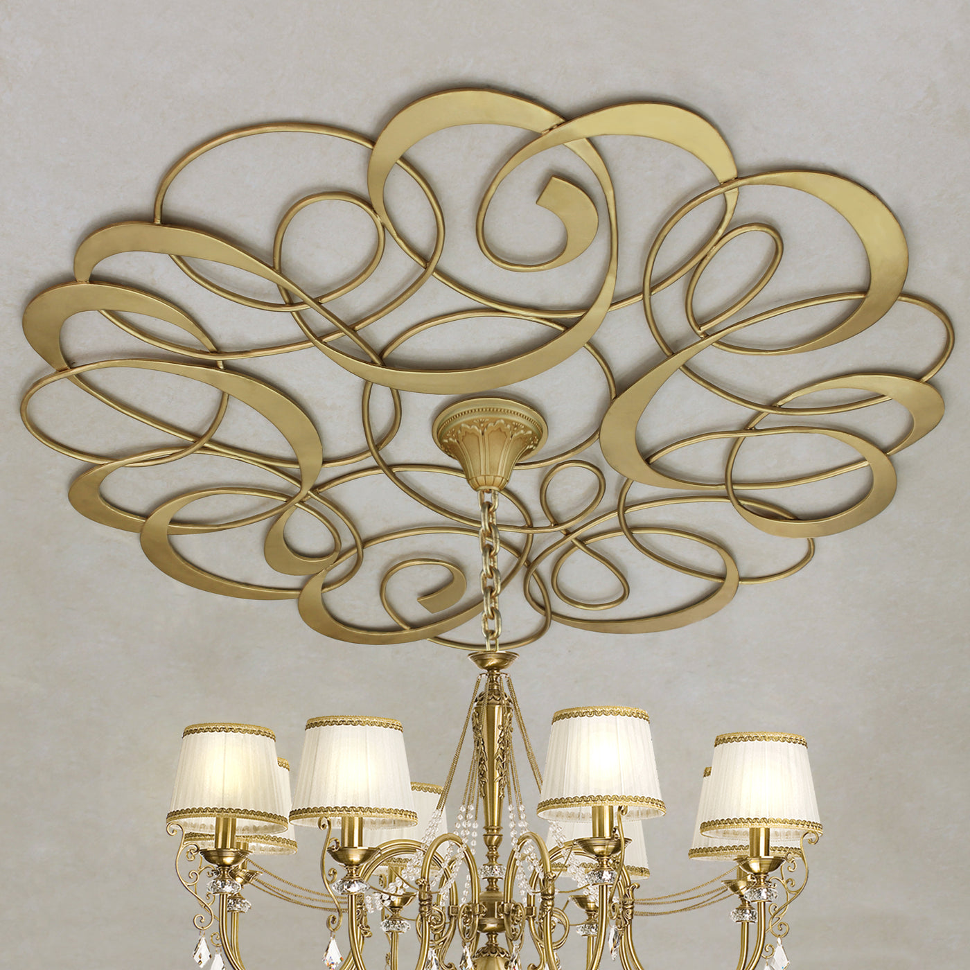 Decorative metal ceiling medallion with an organic pattern and a chandelier hanging from the center; painted in a golden finish