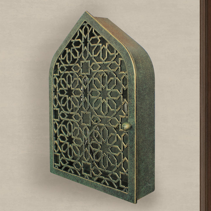A wall mounted closed key cabinet with a geometric pattern and Islamic arched top painted in an antique green-gold finish