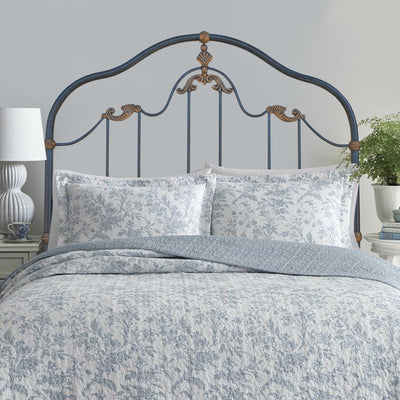 A classical wrought iron single bed with shell motifs painted in an antique blue and gold color; with blue beddings