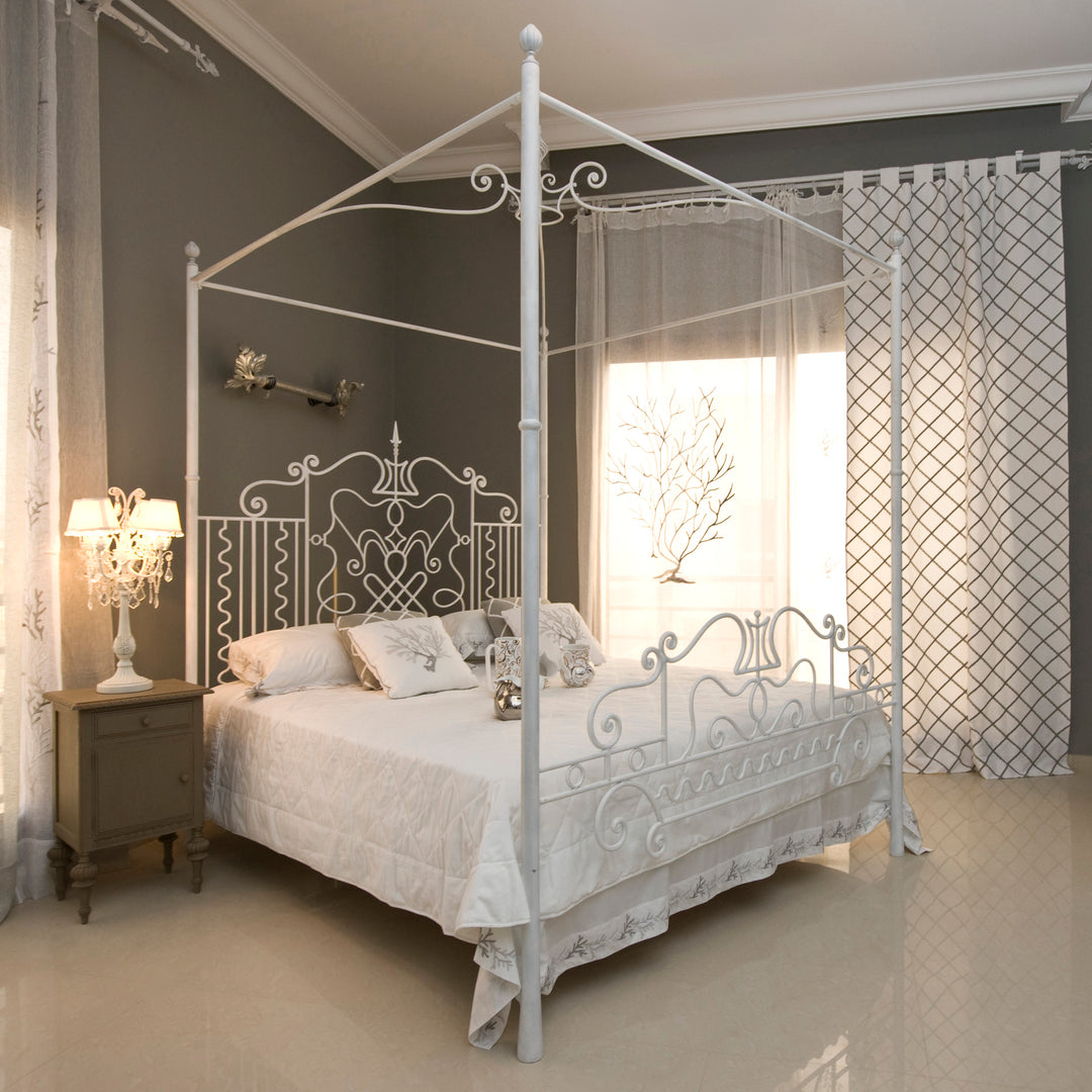 Luxurious wrought iron king sized bed with an overhead canopy painted in white with white beddings