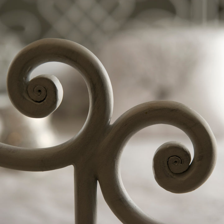 Close up of stylish wrought iron bed footer with scrolls in a white painted finish
