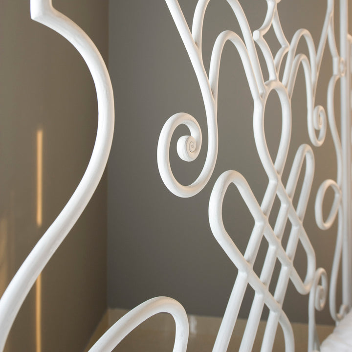 Close up of decorative wrought iron headboard with curves and scrolls in a white painted finish