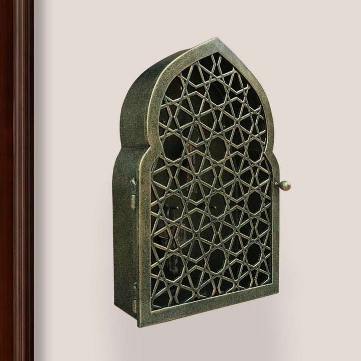 Key cabinet with a geometric pattern and Islamic arched top painted in an antique green-gold finish mounted on a wall beside a wooden door