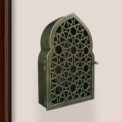 Key cabinet with a geometric pattern and Islamic arched top painted in an antique green-gold finish mounted on a wall beside a wooden door